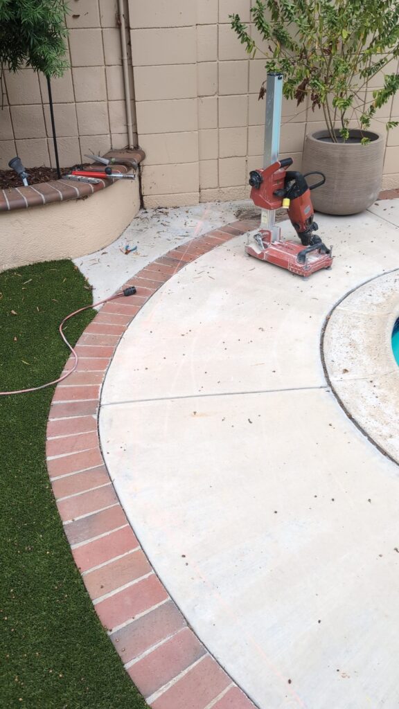 Core drill set up on a concrete pool deck with the fence layout line marked along the brick border