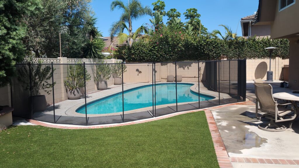 Finished black mesh pool fence following the curve of a concrete pool deck beside artificial turf