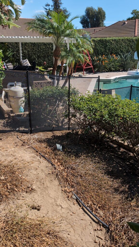 Black mesh pool fence installed in a dirt planter bed near the pool equipment