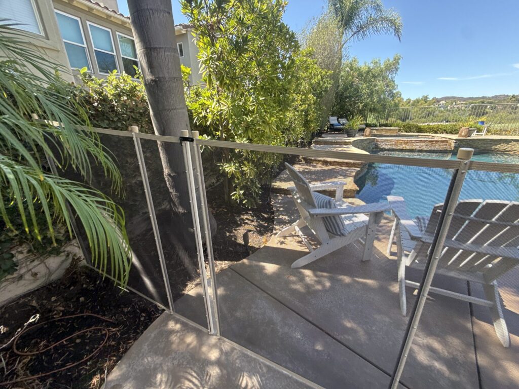 Beige mesh pool fence and gate routed around a palm tree on a concrete deck