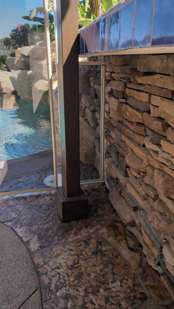 Narrow mesh pool fence section closing the gap between a wood post and a stone wall