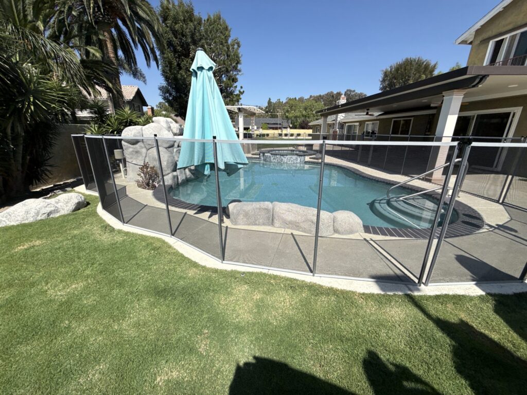Gray mesh pool fence following a curved concrete deck edge beside the lawn