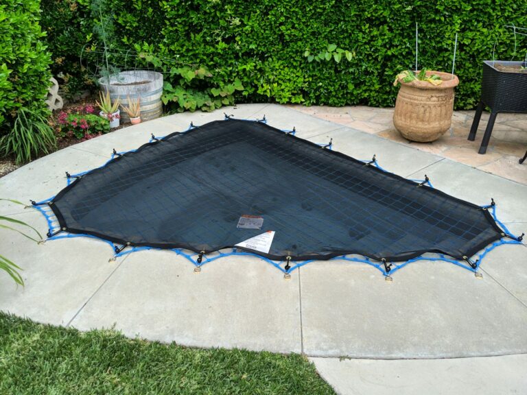 Black leaf cover stretched over a freeform pool in a landscaped backyard