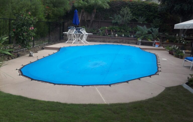Blue leaf cover anchored over a kidney-shaped pool on a concrete deck