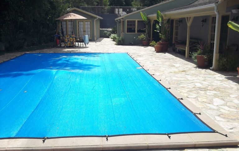 Blue leaf cover pulled tight over a rectangular pool on a flagstone deck