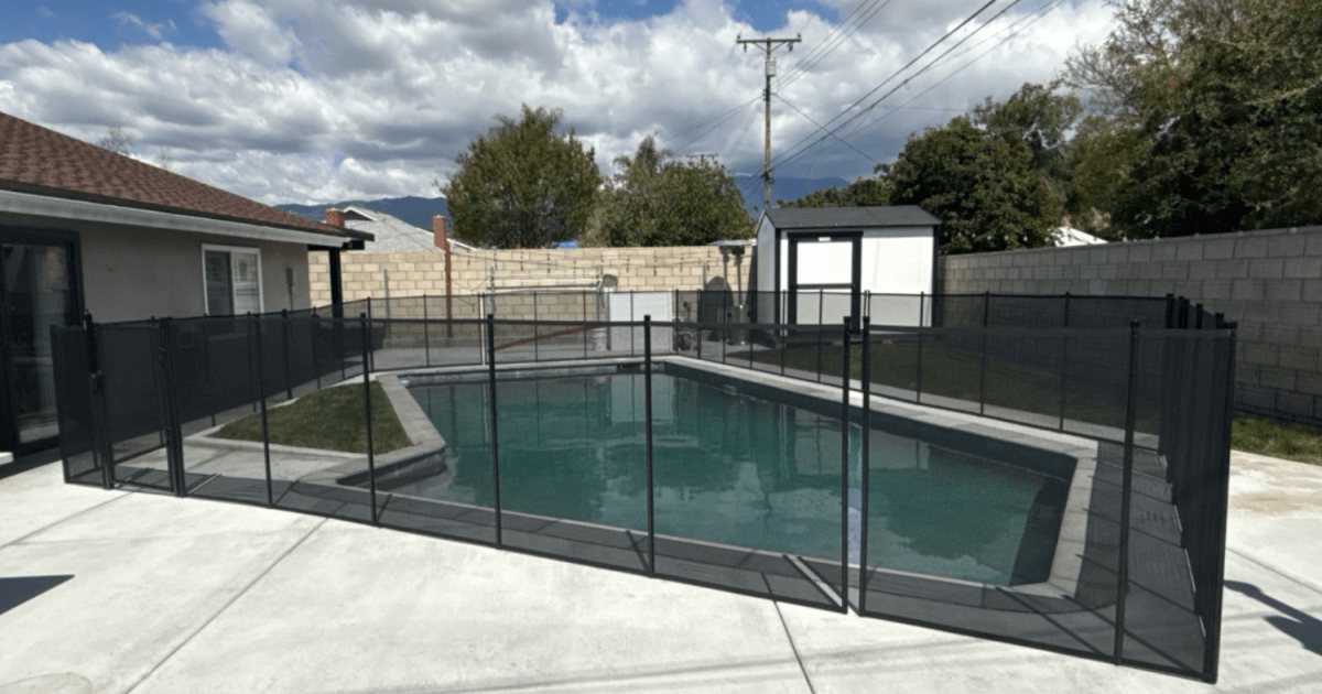 Backyard swimming pool with a black mesh removable pool fence installed surrounding it