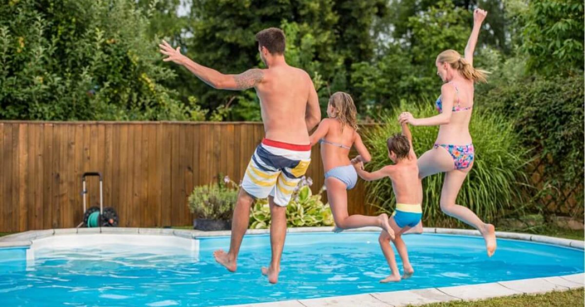 A family of four holding hands as they jump into a swimming pool