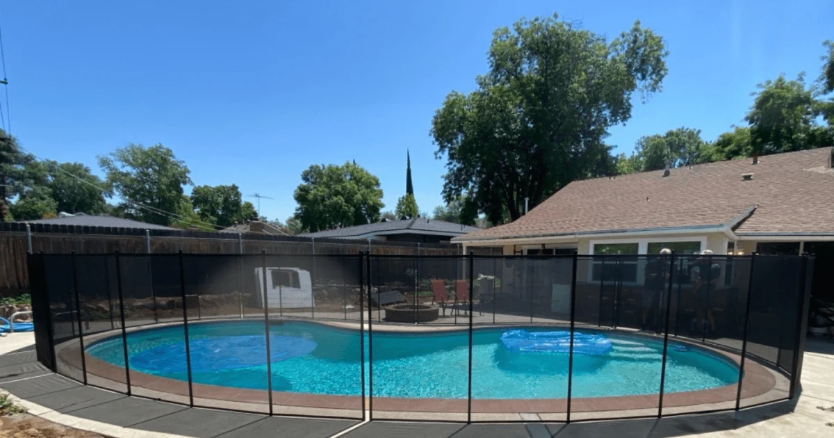 Backyard swimming pool with black mesh pool fence surrounding it and solar sun rings floating in the water