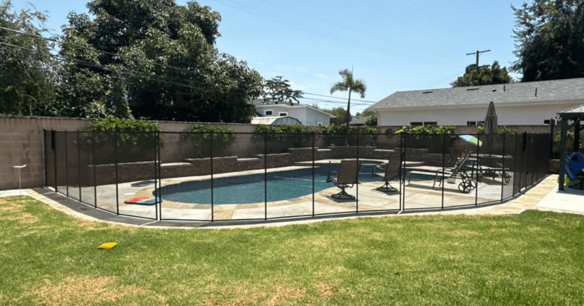 Black mesh pool fence surrounding a swimming pool and patio furniture set