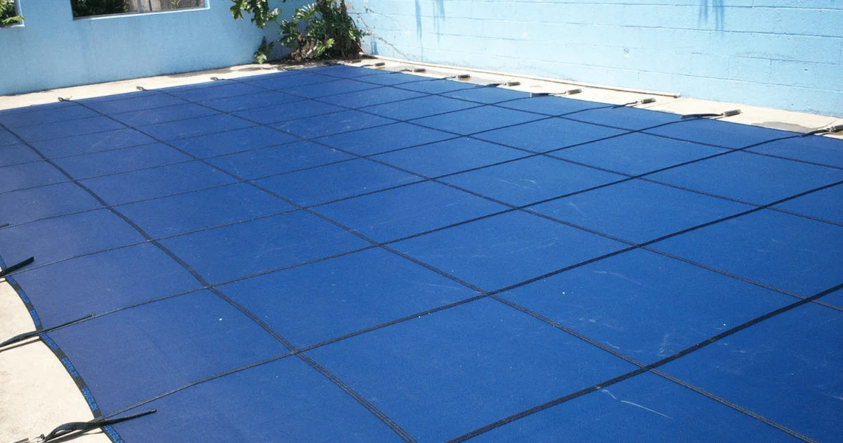 Blue mesh winter pool cover installed over a backyard swimming pool