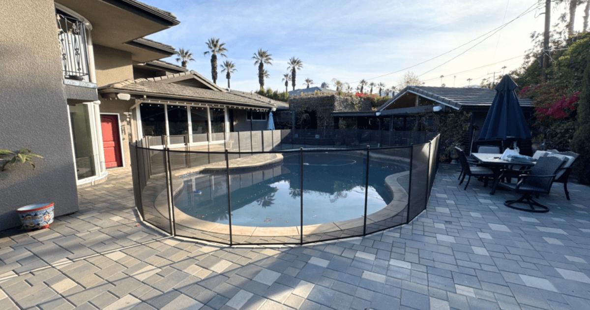 Large backyard patio and swimming pool surrounded by a black mesh removable pool fence