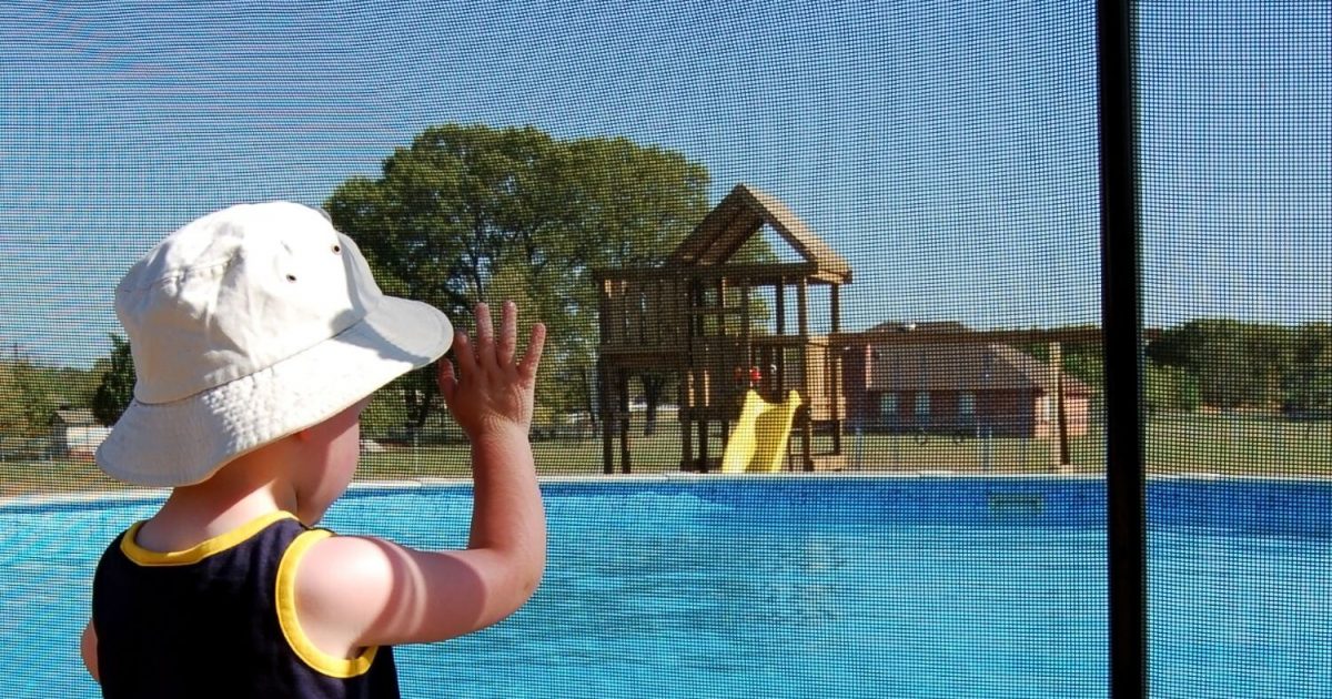 Small child standing outside a mesh pool fence