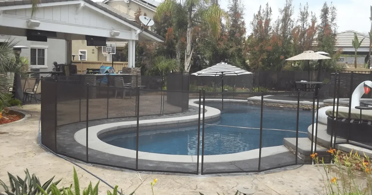 Swimming pool in a back yard with a mesh safety fence around it