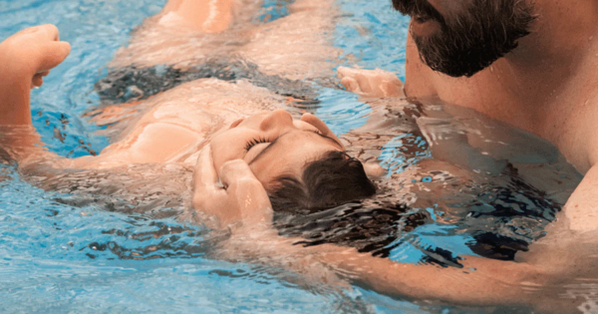 man holding the head of a child while in a pool during aquatic therapy