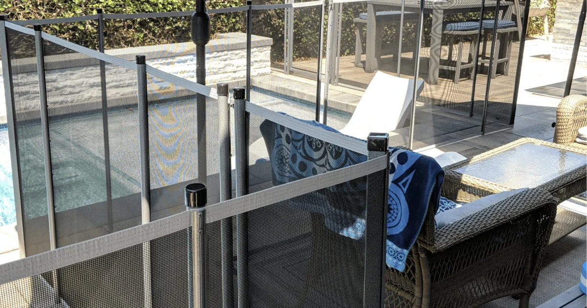 Mesh pool fence around a backyard pool with seating area.