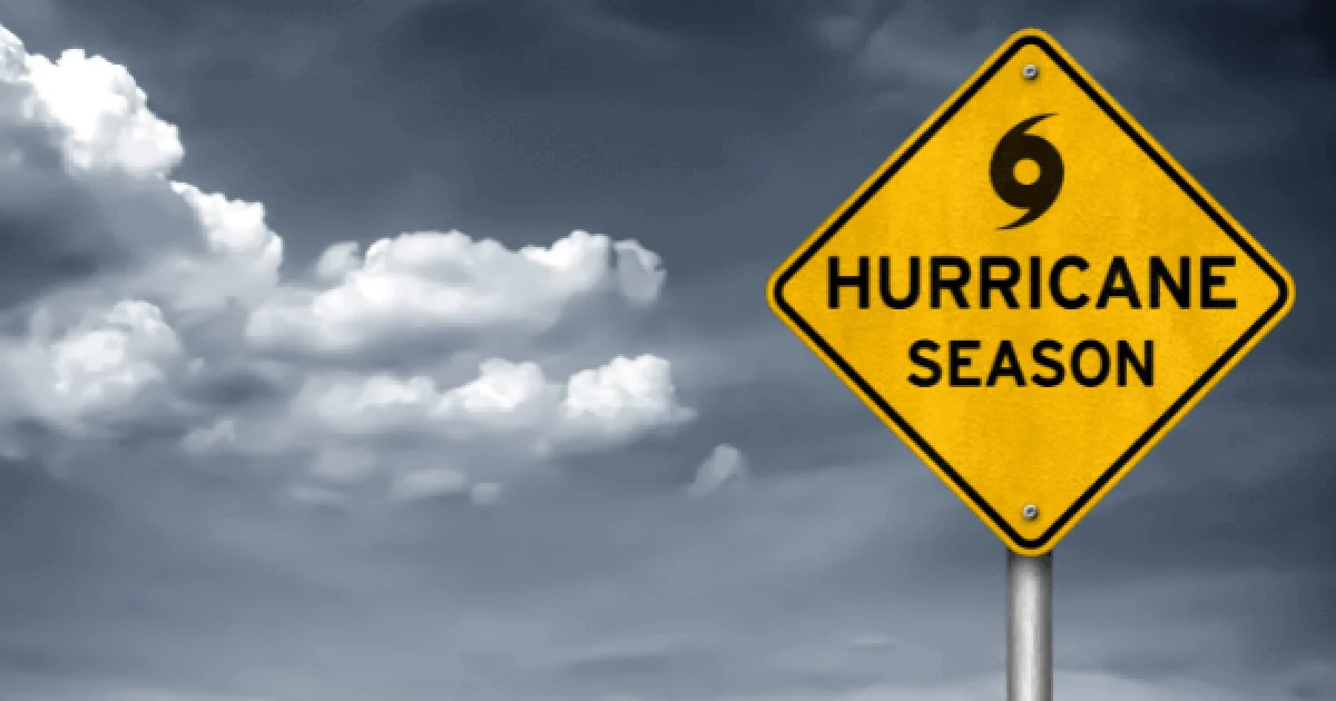 bright yellow road sign reading 'hurricane season' with a background of cloudy skies