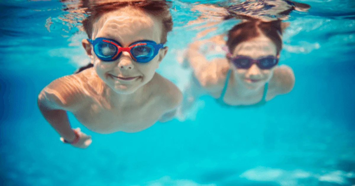 two children swimming in a pool with goggles on
