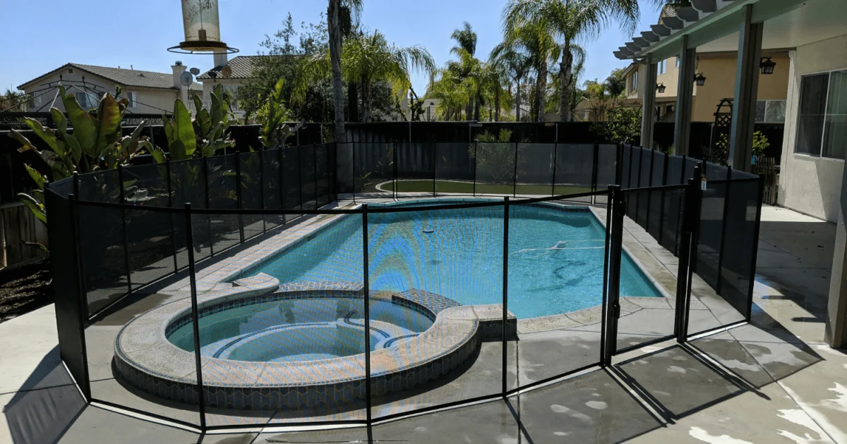 Backyard pool and hot tub surrounded by a black mesh pool fence.