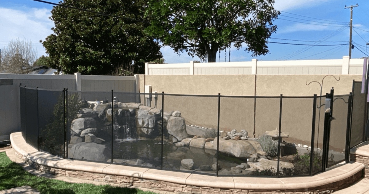 A small backyard pool with a rock waterfall surrounded by a mesh safety fence.
