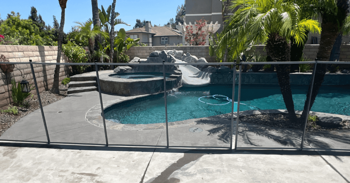 A concrete pool deck with palm tree landscaping and a mesh safety fence installed.