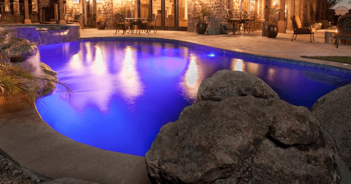 irregular backyard pool with pool lights illuminating the water