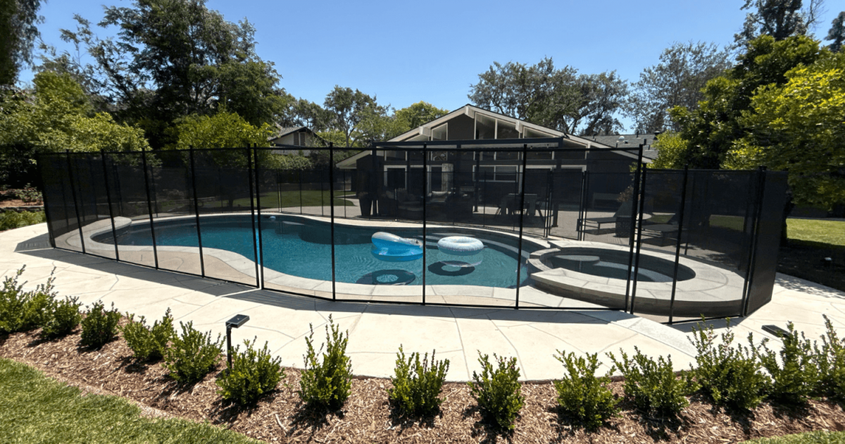 black mesh pool fence surrounding a swimming pool with beautiful landscaping around it