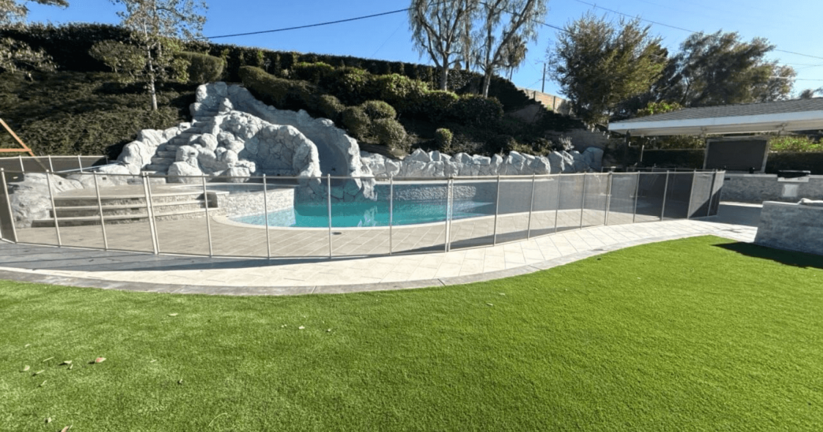 A backyard pool with a large rock water slide feature and pool safety fence around it.