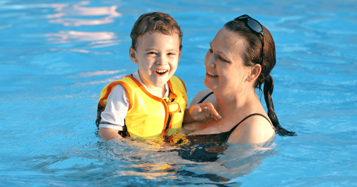 woman in swimming pool holding a boy in a yellow vest
