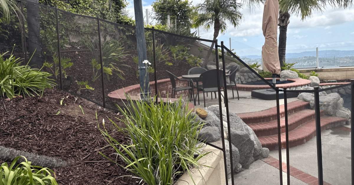 black mesh removable pool fence installed in a sloping backyard with various elevation changes