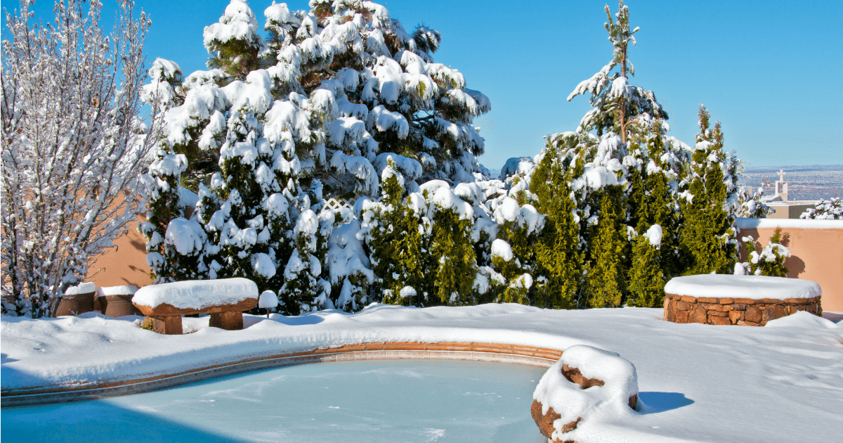 A backyard swimming pool and deck covered in snow after a snowstorm