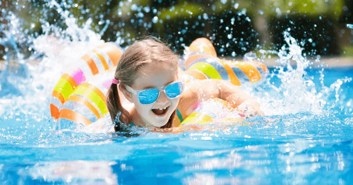 young girl wearing sunglasses on a pool float splashing in the pool